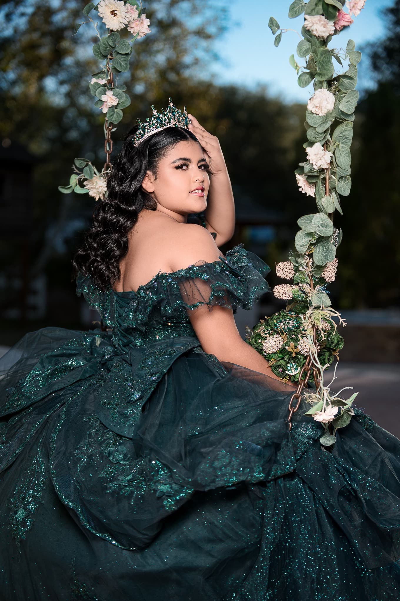 Quinceañera en columpio floral con vestido verde esmeralda